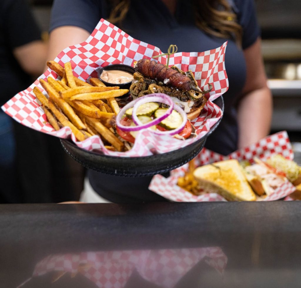 Server holding food in baskets including open-face burger, fries.