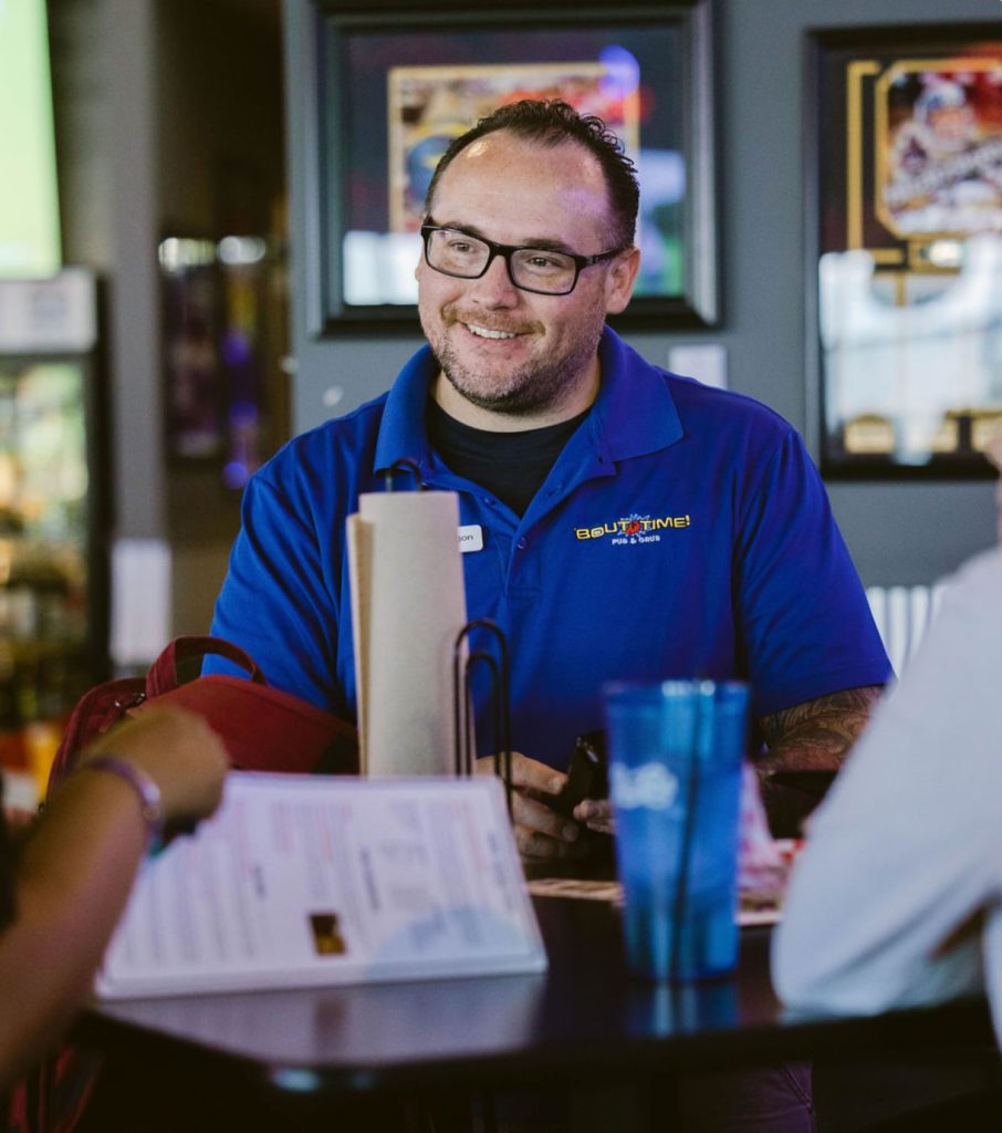 Bout Time Pub & Grub employee waiter smiling while taking customer order.