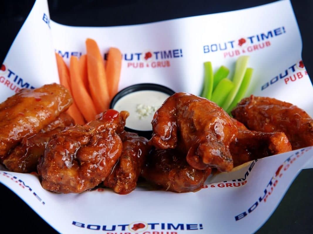 basket of chicken wings with sauce on them. Wings are served with celery and carrot sticks and blue cheese.